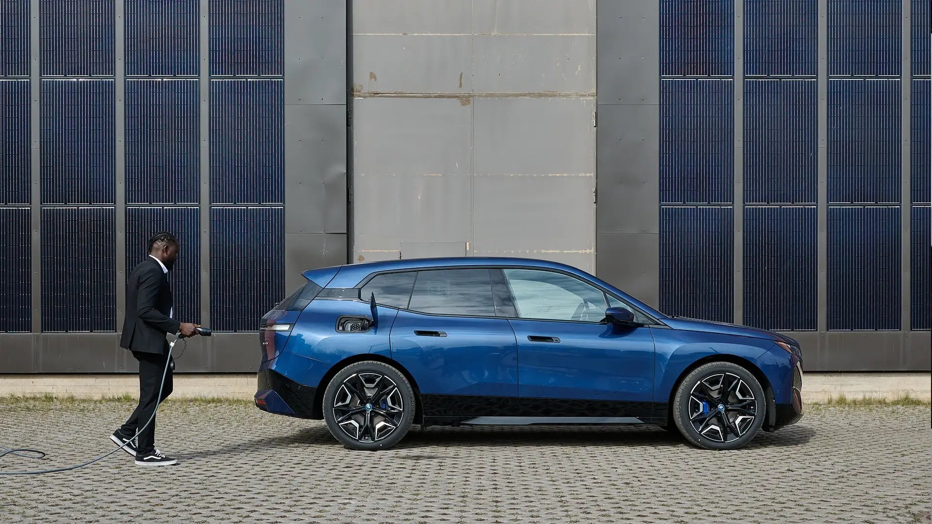 Businessman charging blue electric vehicle beside urban building