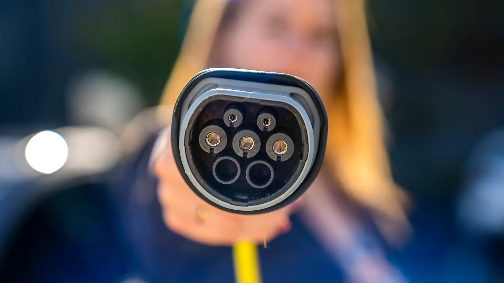 Frau hält Typ Ladestecker eines E-Autos in die Kamera