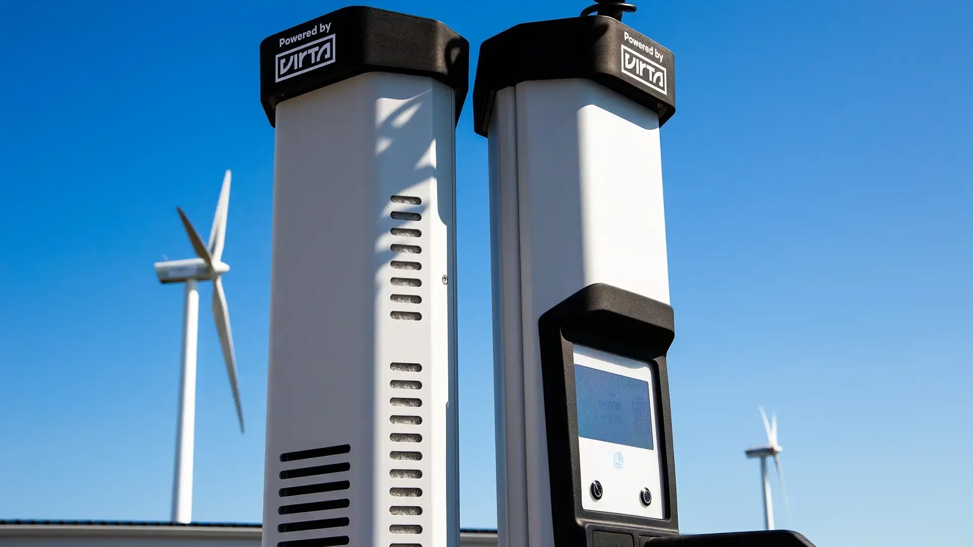 Close-up of a high-power charging station with two wind turbines against a blue sky