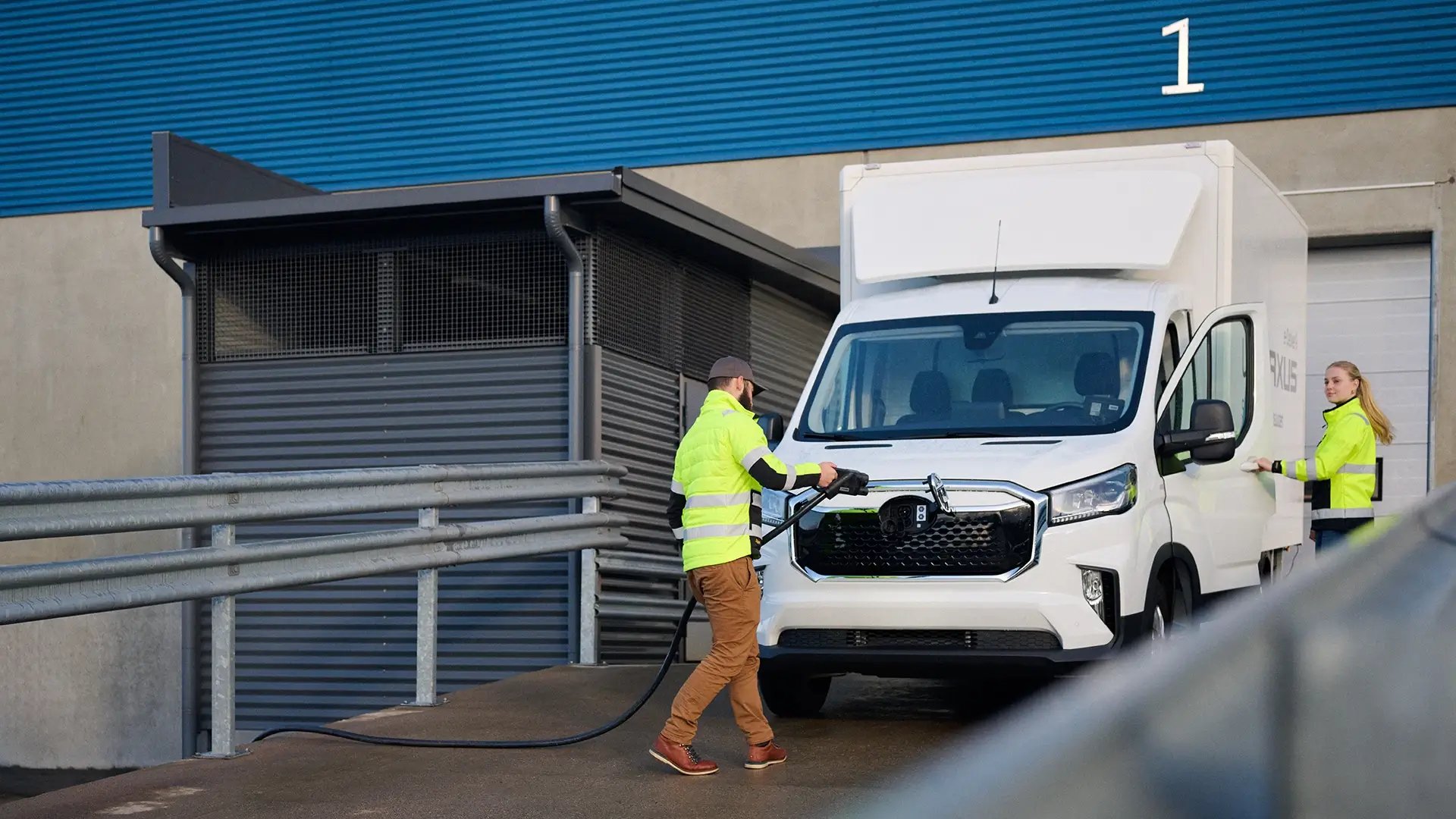 Man and woman charging last mile electric truck outside logistics hub