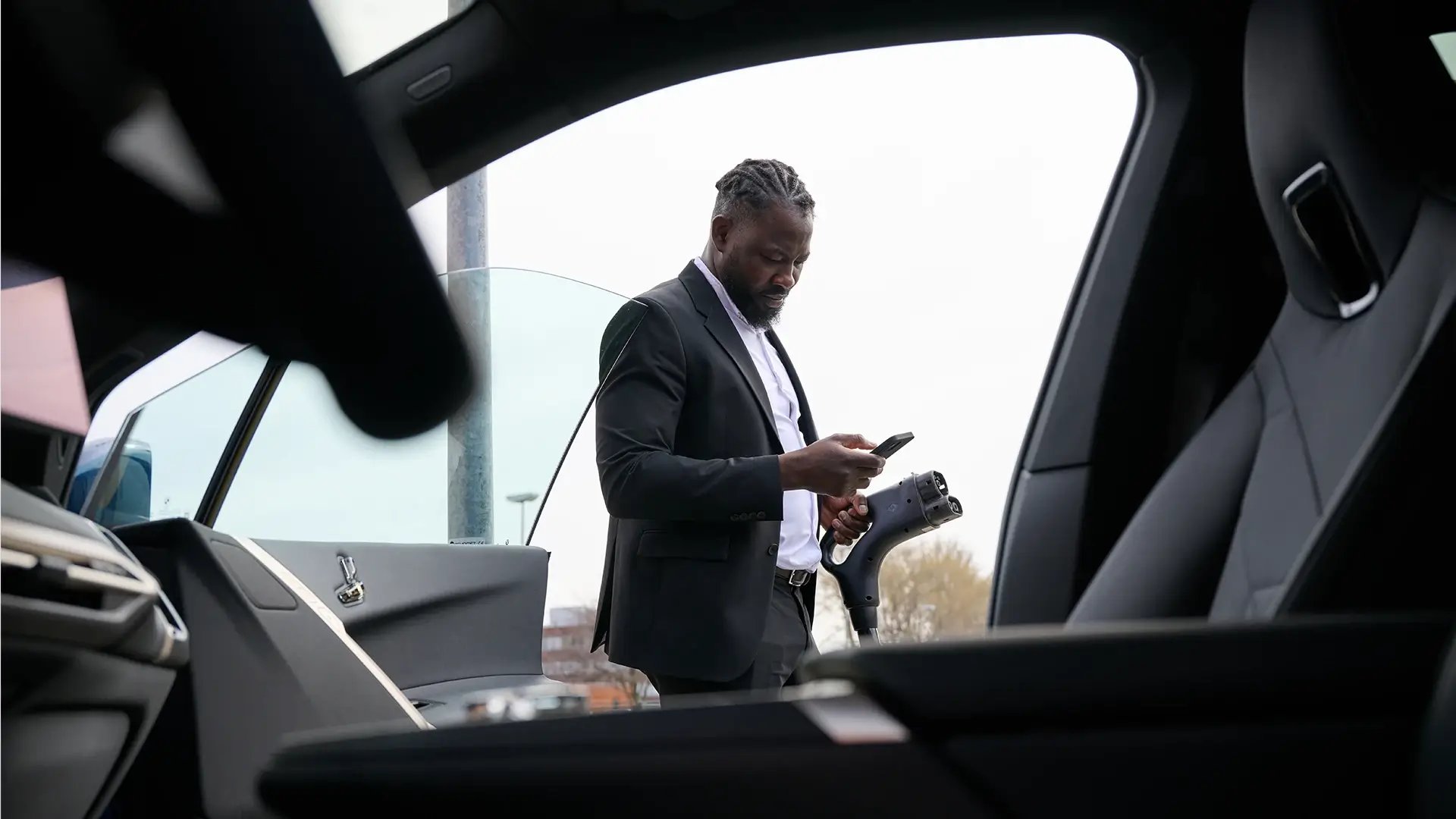 Man using smartphone while holding CCS charging connector in one hand