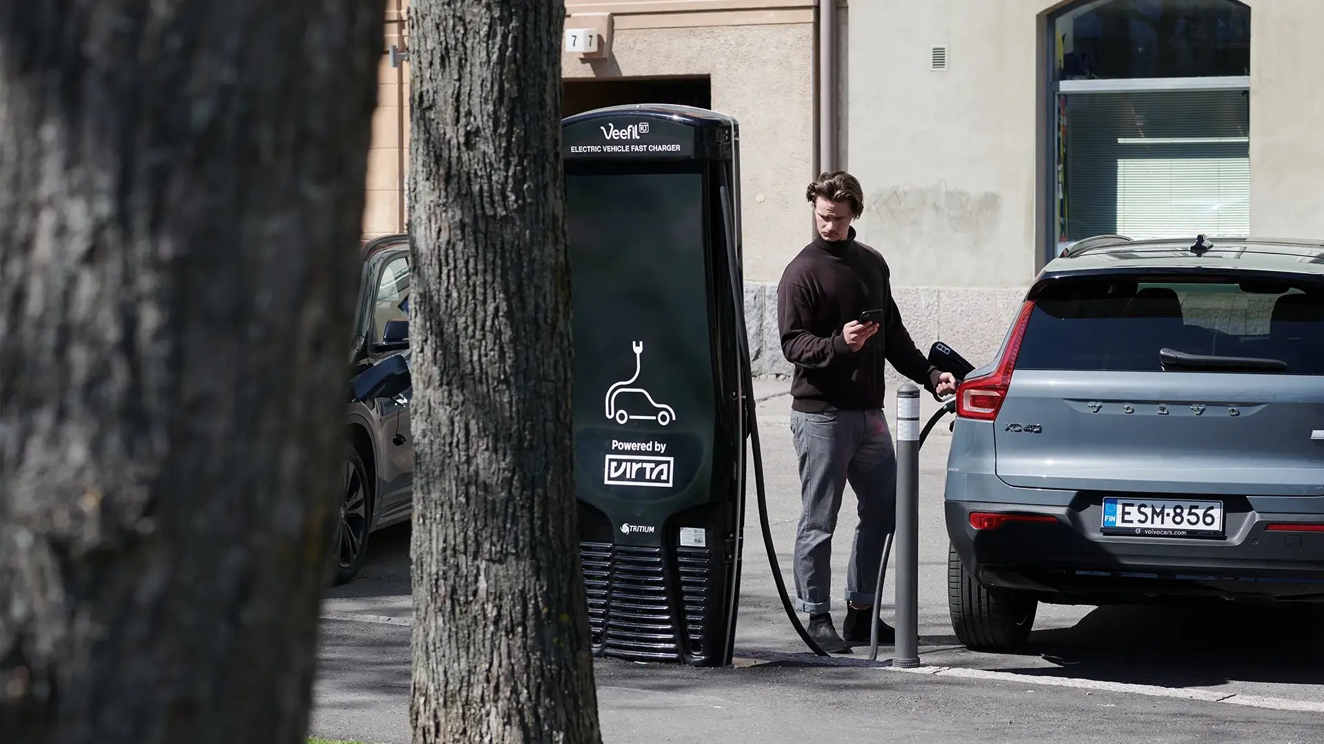 Mann steht neben Ladestation und lädt E-Auto