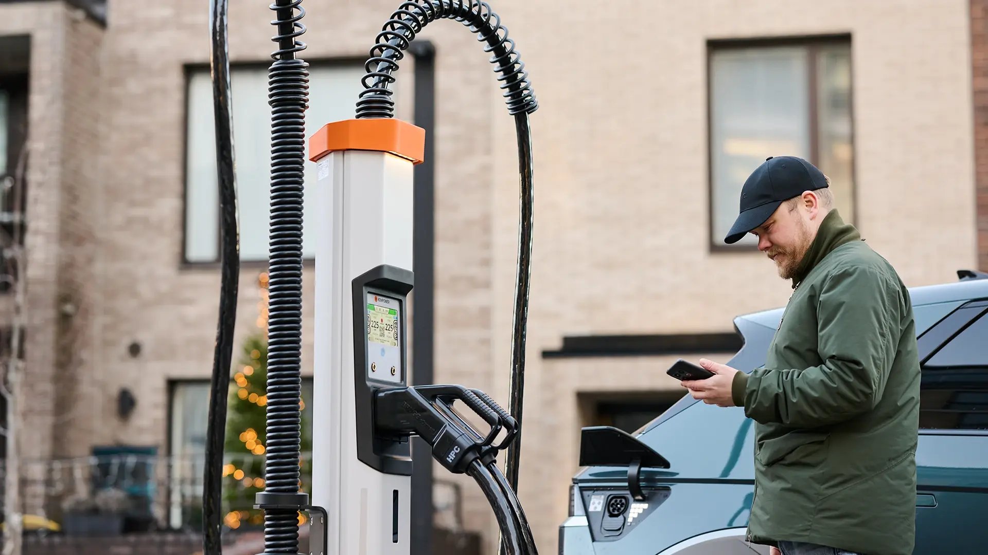 Man wearing a cap looks at his phone in front of HPC charger in residential area