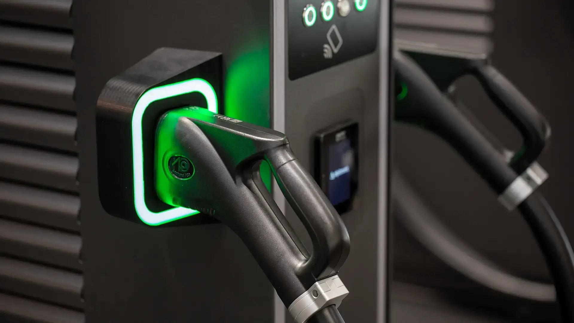 Front view of Phoenix Contact HPC charging handle plugged into ultra-fast EV charger with green LED lighting and cooling vents in background, illustrating high-power charging in action