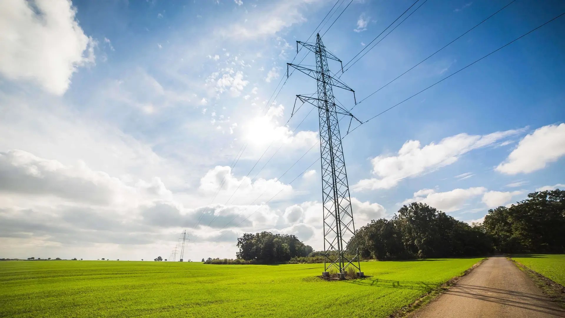 Power transmission lines over green field blue sky