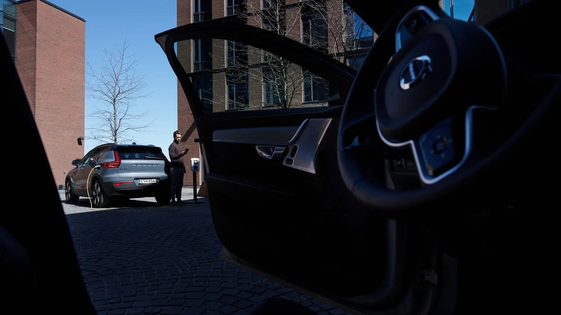 View from inside a car with an opend door showing man charging EV