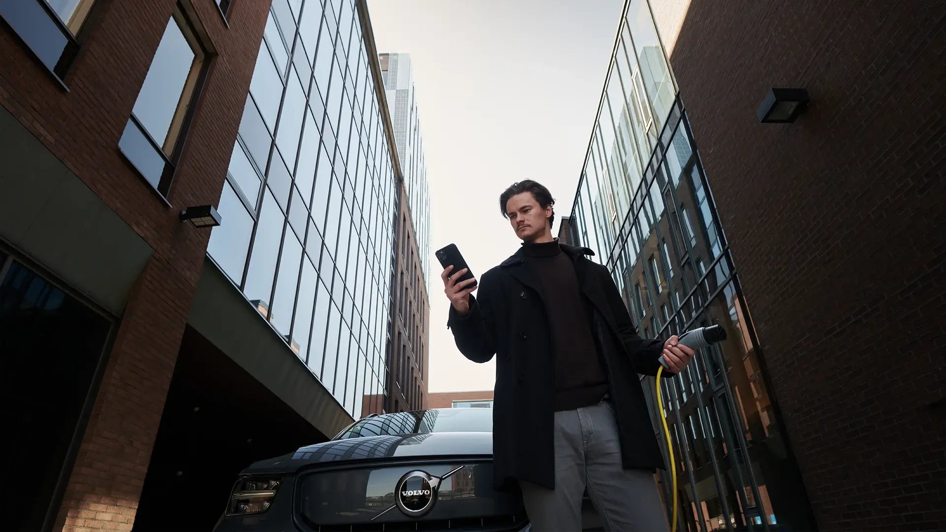 Man managing EV charging via smartphone app with charging cable in his hand