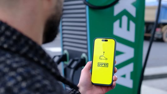 Mann hält Smartphone in Hand mit offener Virta App für das Laden im Hintergrund Alpitronic Hypercharger HYC 400 Ladestation im AVEX Schnellladepark in Euskirchen