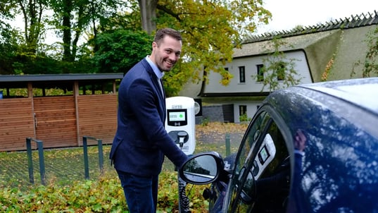 Mann hält Ladekabel an E-Auto
