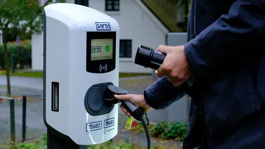 Man standing with an AC charging connector at an AC charger