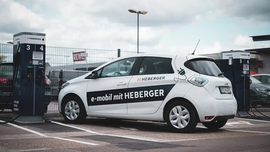 Ein elektrisches Dienstfahrzeug von HEBERGER steht zwischen zwei DC-Ladestationen zwischen zwei DC-Ladegeräten auf einem Parkplatz