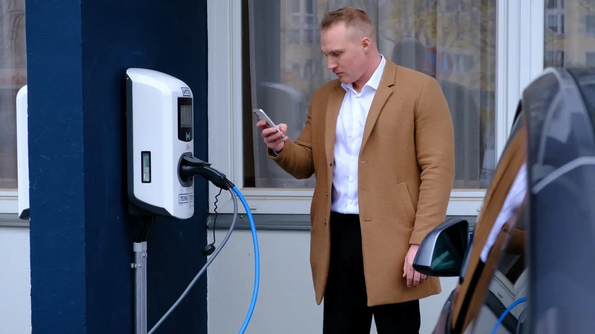 Mann mit Smartphone lädt E-Auto an Alfen Ladestation am Hotel Berlin Berlin Teil der Pandox Gruppe