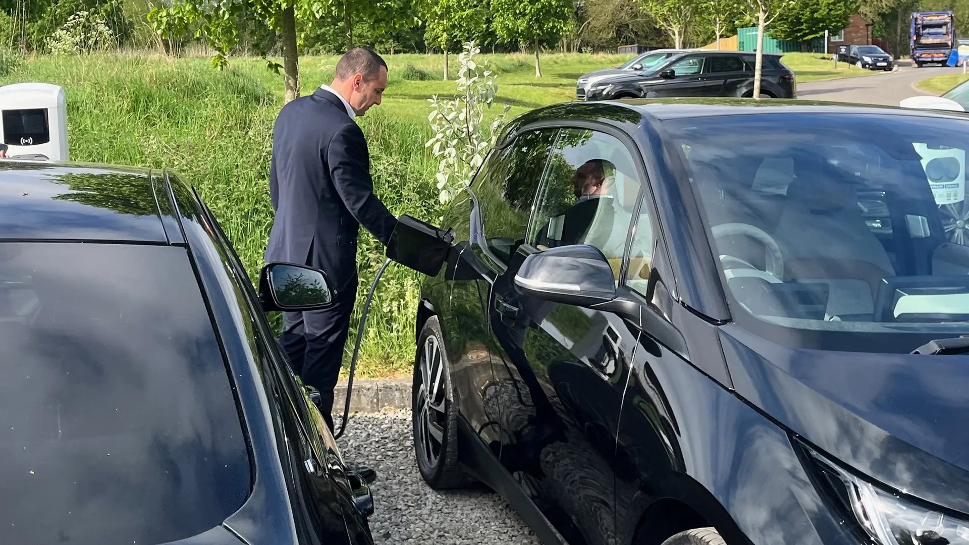 man-charging-ev-next-to-a-green-field