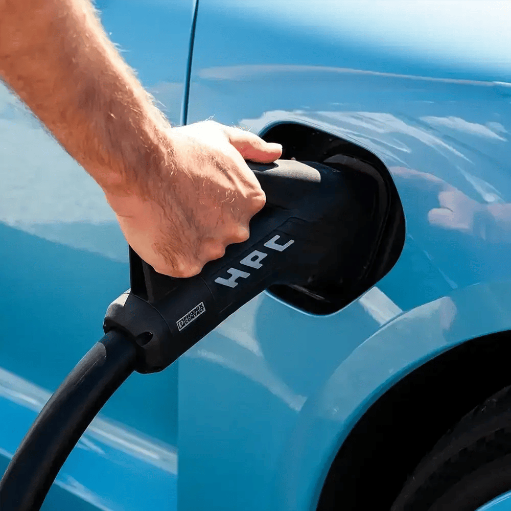 Sininen EV ja HPC-latausaseman liitintä pitelevä mies