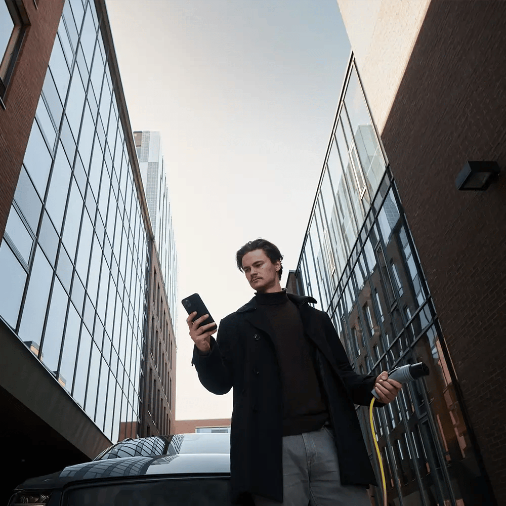 Man beheert opladen van EV via smartphone-app met oplaadkabel in zijn hand
