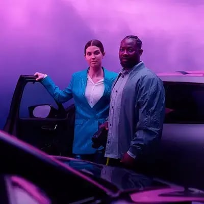 Nainen ja mies lataamassa sähköautoa violetilla taustalla
