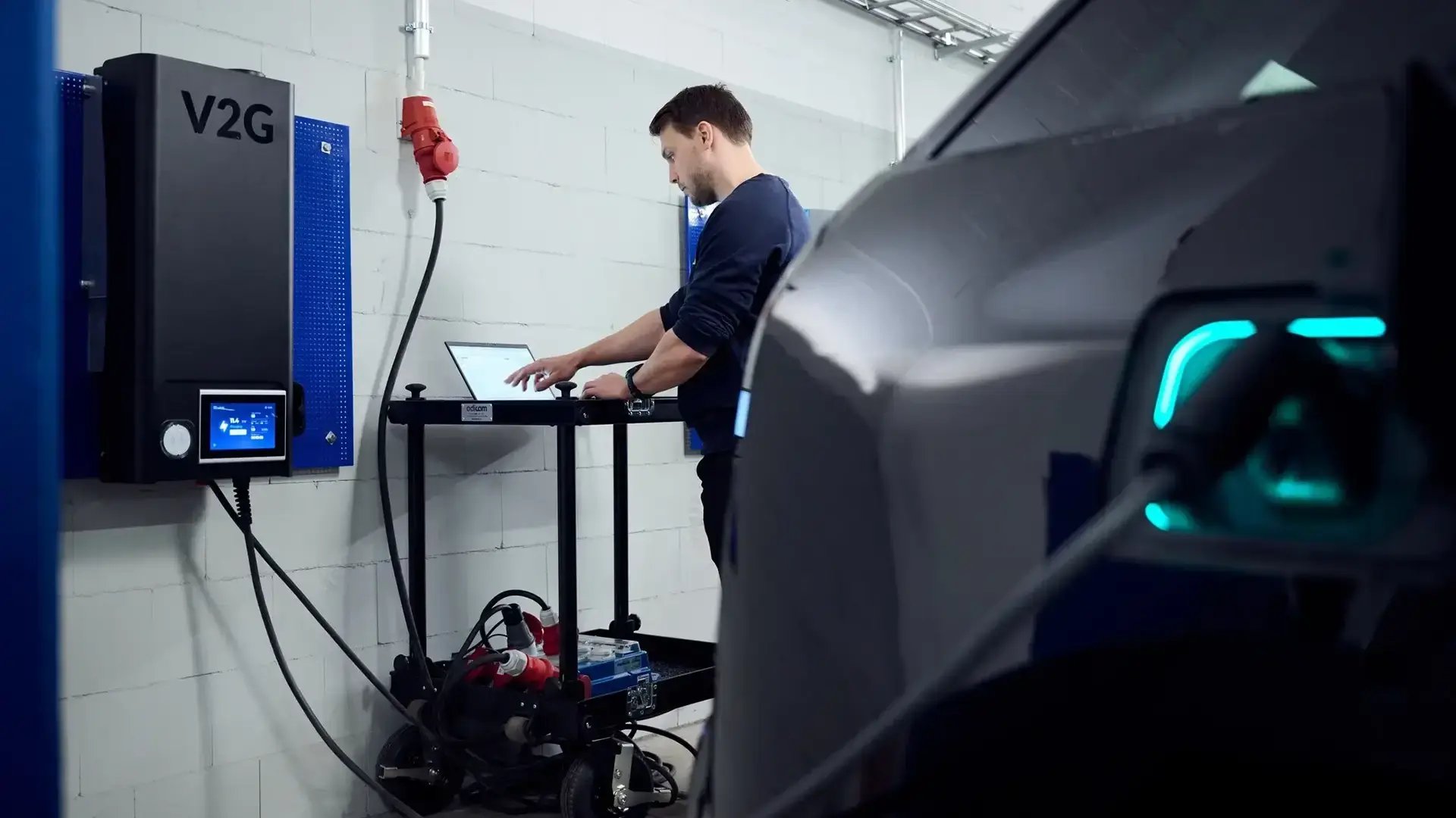 Man working at a computer in a garage next to V2G charger