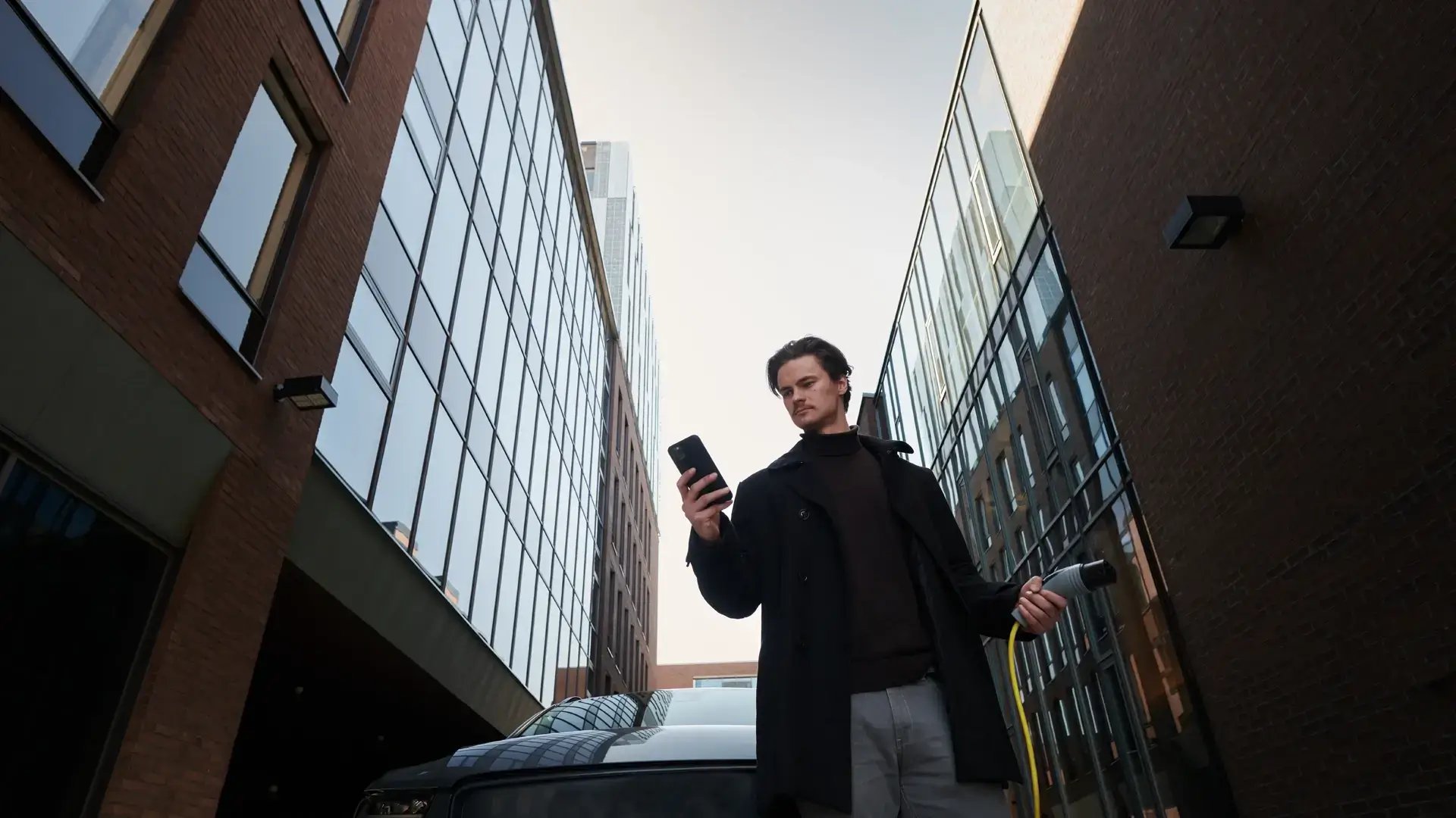 Man managing EV charging via smartphone app with charging cable in his hand