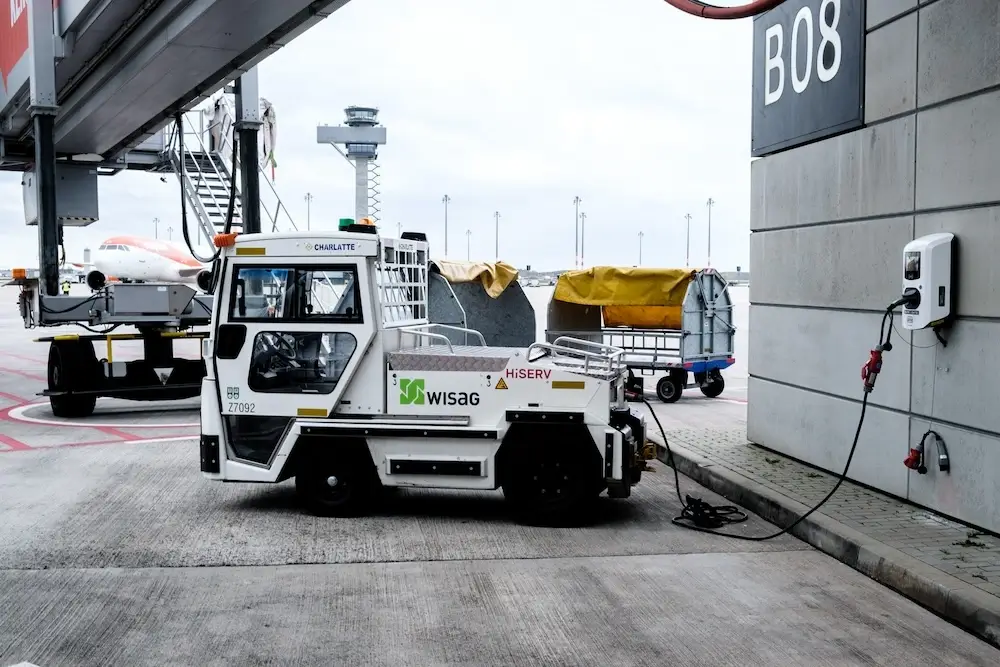 Elektrisches Zugfahrzeug für den Transport von Waggons am Vorfeld des Flughafens BER Berlin Brandenburg wird an der Luftgastbrücke an einer Virta Ladestation geladen