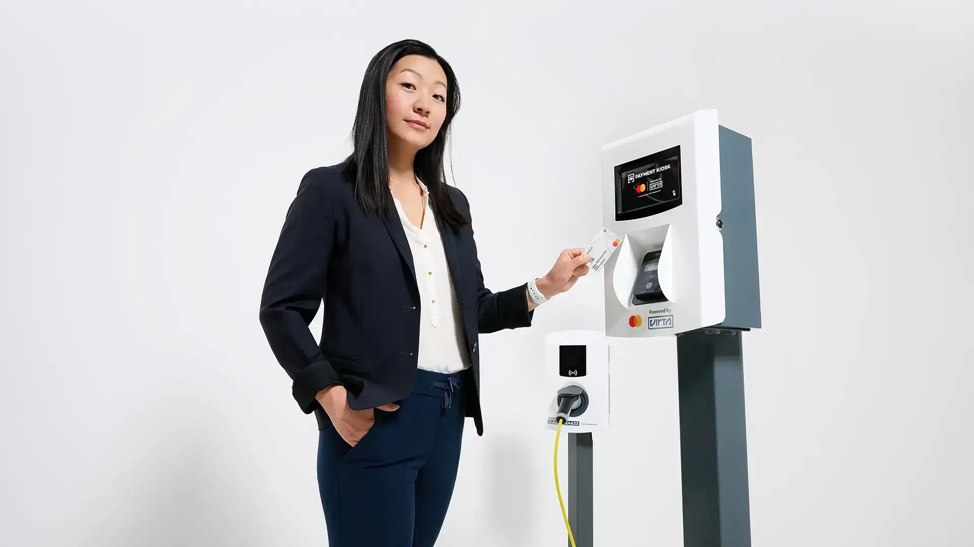 Kvinne står ved siden av Virta Payment Kiosk og en AC-lader